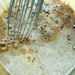 A whisk in a bowl with frothy, brown liquid, likely a mixture of wet and dry ingredients for baking, resembling the savory blend you'd find in a slow cooker Salisbury steak recipe.