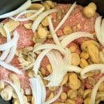 Raw ground beef topped with sliced onions and mushrooms, perfect for transforming into a hearty slow cooker Salisbury steak masterpiece in your pan.
