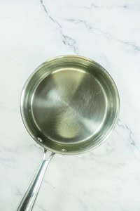 A stainless steel saucepan filled with water sits on a white marble countertop, ready to help prepare ingredients for strawberry pretzel salad.