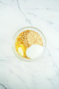 A glass bowl containing sugar, chopped nuts, butter, and egg on a white marble surface—classic ingredients for the perfect strawberry pretzel salad base.