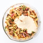 A glass bowl filled with taco pasta salad—rotini pasta, ground beef, beans, red onions, and herbs—all topped with a creamy white sauce.