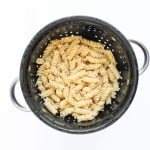 Cooked fusilli pasta for taco pasta salad draining in a black metal colander with handles, viewed from above on a white background.