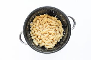 Cooked fusilli pasta for taco pasta salad draining in a black metal colander with handles, viewed from above on a white background.
