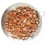 Cooked ground beef seasoned with spices for a flavorful taco pasta salad, shown in a stainless steel skillet from above on a white background.