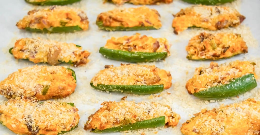 Halved jalapeños filled with a creamy, crumb-topped mixture are arranged on a baking sheet lined with parchment paper, perfect for making Air Fryer Jalapeño Poppers.