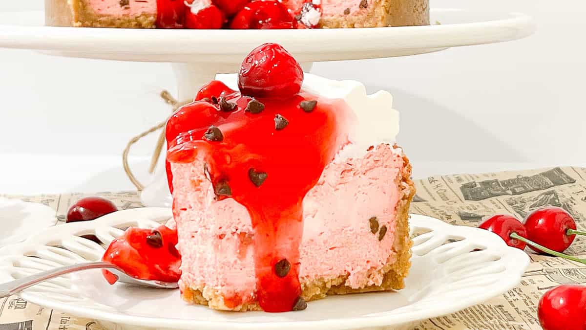 A slice of pink cheesecake with cherries and chocolate chips. 