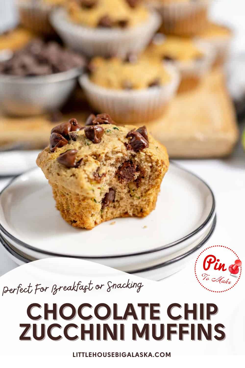 A chocolate chip zucchini muffin with a bite taken out sits on a plate, with more muffins and chocolate chips blurred in the background.