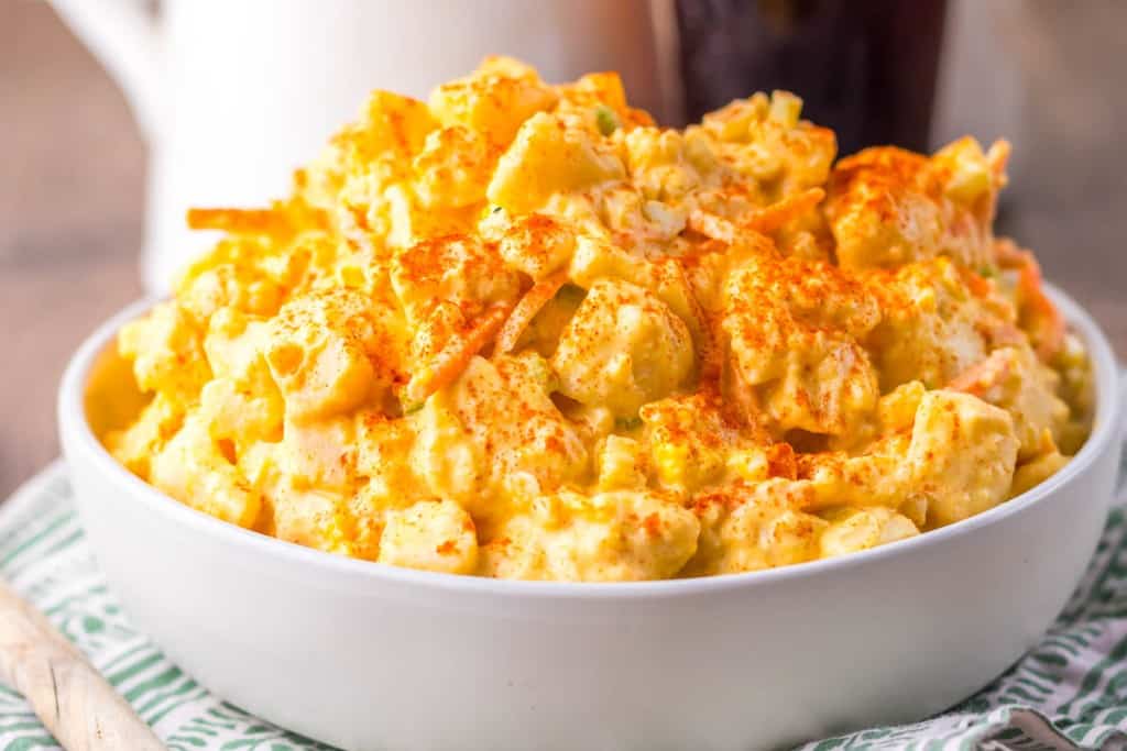 A bowl of potato salad topped with paprika, featuring chunks of potatoes mixed with mayonnaise and shredded carrots.