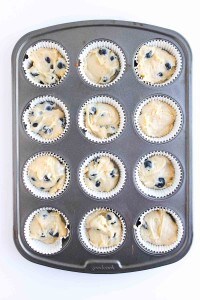 A muffin tin with twelve paper liners filled with raw Blueberry Cheesecake Muffins batter, ready to be baked.