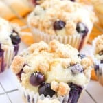 Several Blueberry Cheesecake Muffins with crumb topping are arranged on a cooling rack.