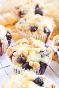 Several Blueberry Cheesecake Muffins with crumb topping are arranged on a cooling rack.