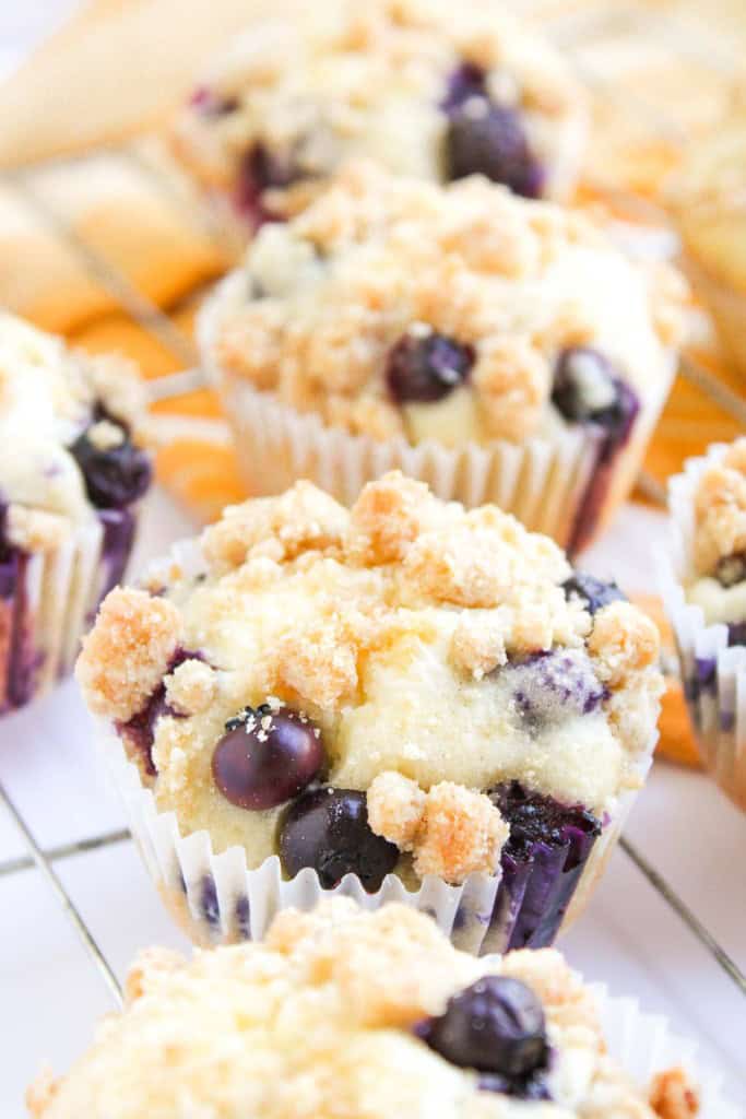 Several Blueberry Cheesecake Muffins with crumb topping are arranged on a cooling rack.