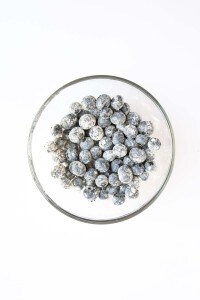 A glass bowl filled with blueberries coated in a layer of white flour, photographed from above on a white background—perfectly prepped for Blueberry Cheesecake Muffins.