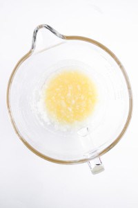 A glass mixing bowl containing melted butter and sugar, the perfect start for baking delicious Blueberry Cheesecake Muffins, sits on a white background.