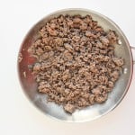 Cooked ground beef in a stainless steel skillet on a white background.
