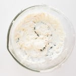 A glass mixing bowl containing whipped cream cheese on a white surface.