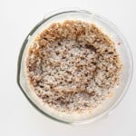 A glass bowl filled with a mixture of cooked oatmeal and chia seeds sits on a white surface, viewed from above.