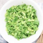 A white bowl filled with Grinder Chopped Salad, featuring crisp green lettuce, sits on a countertop next to a striped cloth and wooden salad utensils.