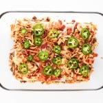 A rectangular glass baking dish containing a layered casserole topped with sliced jalapeños, shredded cheese, and ground meat.