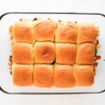 A glass baking dish containing twelve baked slider sandwiches arranged in a 3x4 grid, photographed from above.