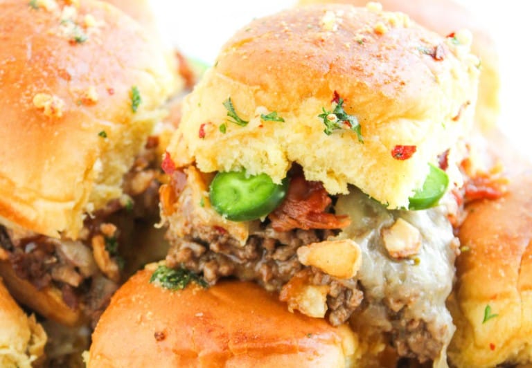 Close-up of Cowboy Sliders featuring ground beef, melted cheese, sliced jalapeños, bacon, and herbs on a golden bun.