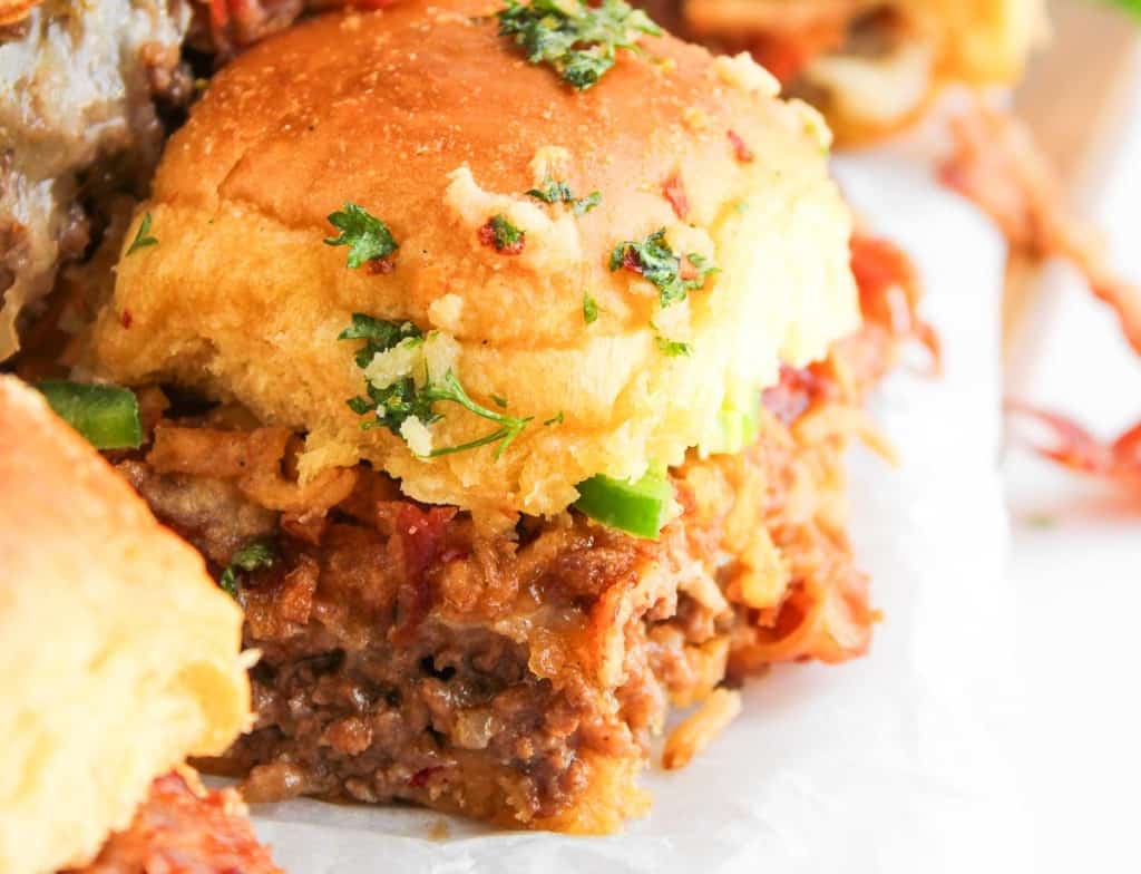 Close-up of Cowboy Sliders: pulled beef sandwiches with melted cheese, herbs, and a golden toasted bun on white parchment paper.