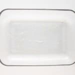 A rectangular glass baking dish with a light coating of butter or oil on the bottom, placed on a white surface.