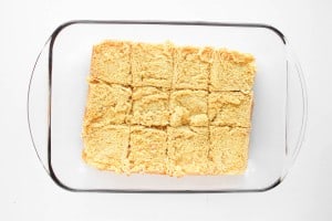 Glass baking dish containing twelve square pieces of cornbread, some with slightly uneven edges, on a white background.