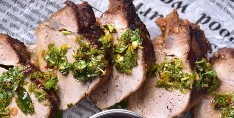 Sliced grilled meat from our Sizzling Grill recipes, garnished with chopped herbs and served on a sheet of newspaper-style paper.