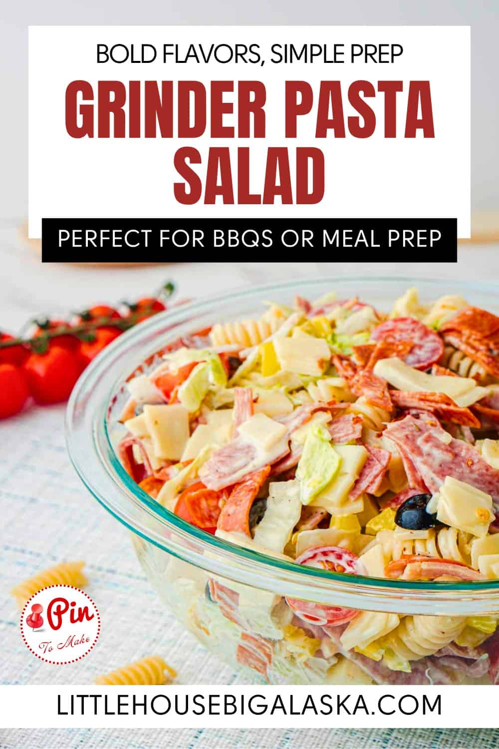 A glass bowl filled with grinder pasta salad is placed on a white surface, with a tomato and a cloth nearby; text promotes the salad for BBQs or meal prep.