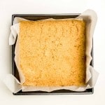 A square, golden-brown baked crust sits in a parchment-lined metal baking pan on a white background.