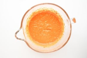 A glass mixing bowl filled with orange batter or sauce, shown from above on a white background.