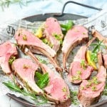 A round tray lined with newspaper holds six slices of succulent rack of lamb, garnished with fresh herbs and lemon wedges.