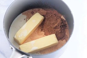 Two sticks of butter, cocoa powder, and liquid cream in a saucepan, ready to be mixed and heated.