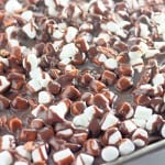 A close-up of a tray filled with chocolate-drizzled marshmallows and pecans, likely freshly made rocky road dessert.