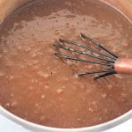 A metal whisk is in a pot of bubbling chocolate pudding being stirred.