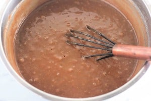 A metal whisk is in a pot of bubbling chocolate pudding being stirred.