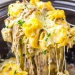 A close-up of cheesy tortellini pasta being lifted with a spoon, topped with melted cheese and sprinkled with chopped herbs—perfect for fans of Slow Cooker recipes.