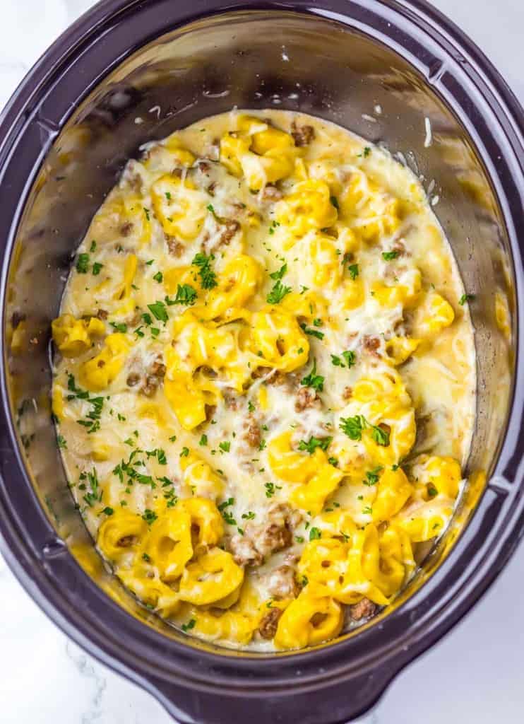 Cheese tortellini, ground sausage, and creamy sauce cooked together in a slow cooker, topped with chopped parsley.