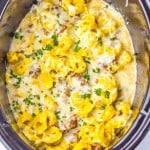 Cheese tortellini, sausage, and creamy sauce garnished with chopped parsley in a slow cooker.