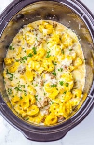 Cheese tortellini, sausage, and creamy sauce garnished with chopped parsley in a slow cooker.