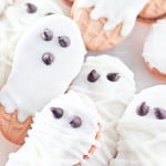 Halloween cookies decorated as mummies and ghosts with white icing and chocolate chip eyes, arranged closely together on a light surface.