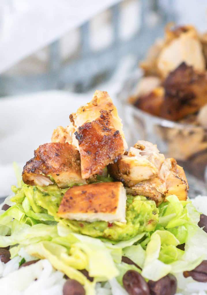 Grilled chicken pieces on top of guacamole, shredded lettuce, black beans, and rice.