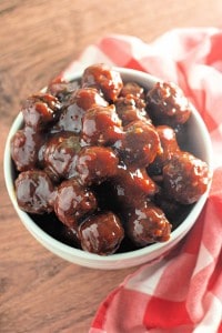 A white bowl filled with Slow Cooker Hot Honey Meatballs sits on a wooden surface next to a red and white checkered cloth.