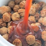 A close-up of Slow Cooker Hot Honey Meatballs as rich sauce is poured over a pile of meatballs in a white bowl or slow cooker.
