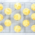 Fourteen golden muffins cool on a metal wire rack, arranged in a grid pattern on a white marble surface.