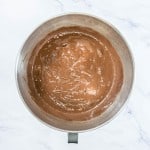 A stainless steel mixing bowl filled with smooth chocolate cake batter on a white marble surface.