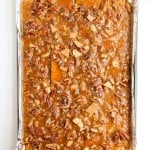 A rectangular baking sheet lined with foil holds a layer of pecan praline bark with visible pecans and graham crackers in a caramel coating.