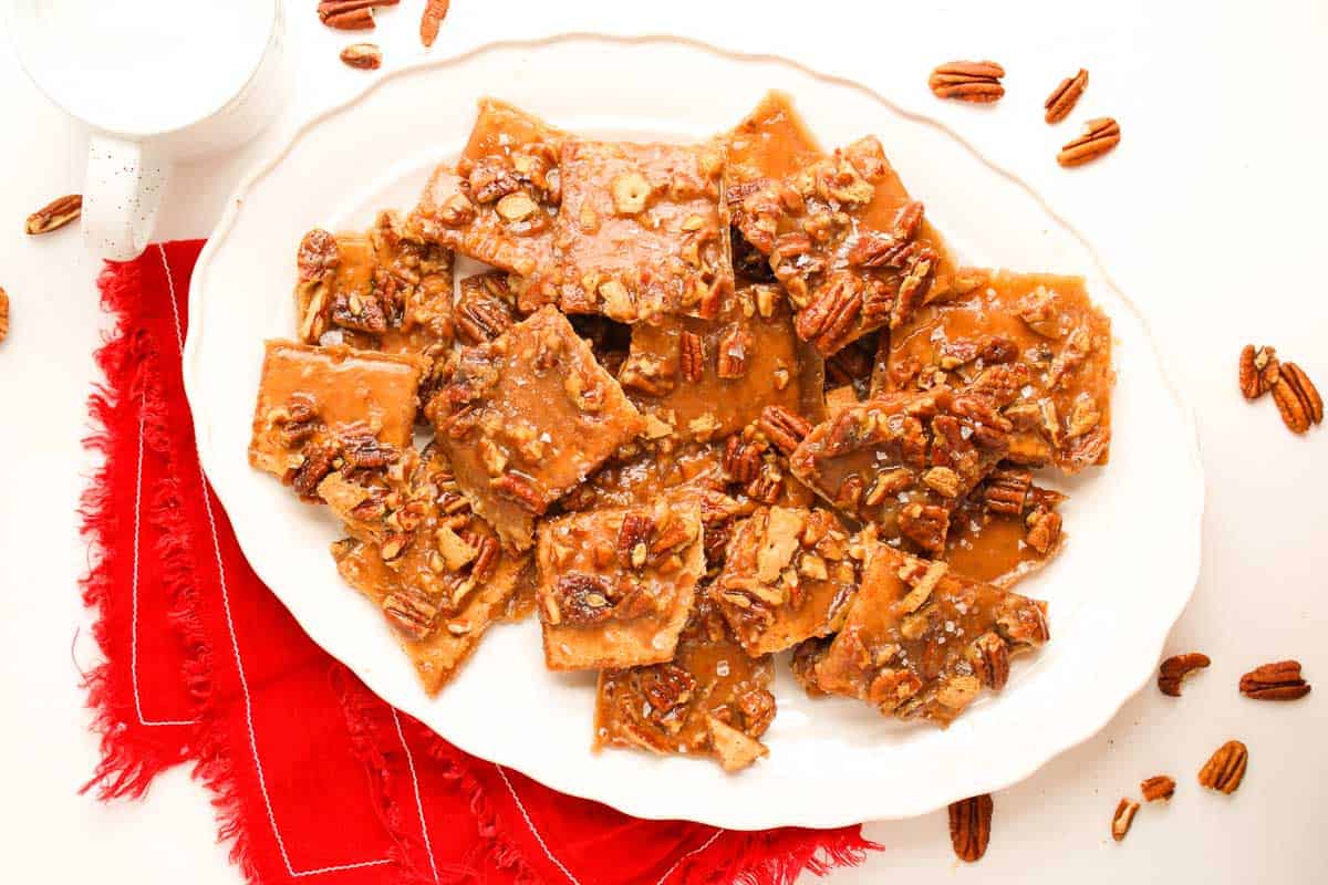 Plate of pecan pie bark pieces topped with caramel and chopped pecans on a red napkin.