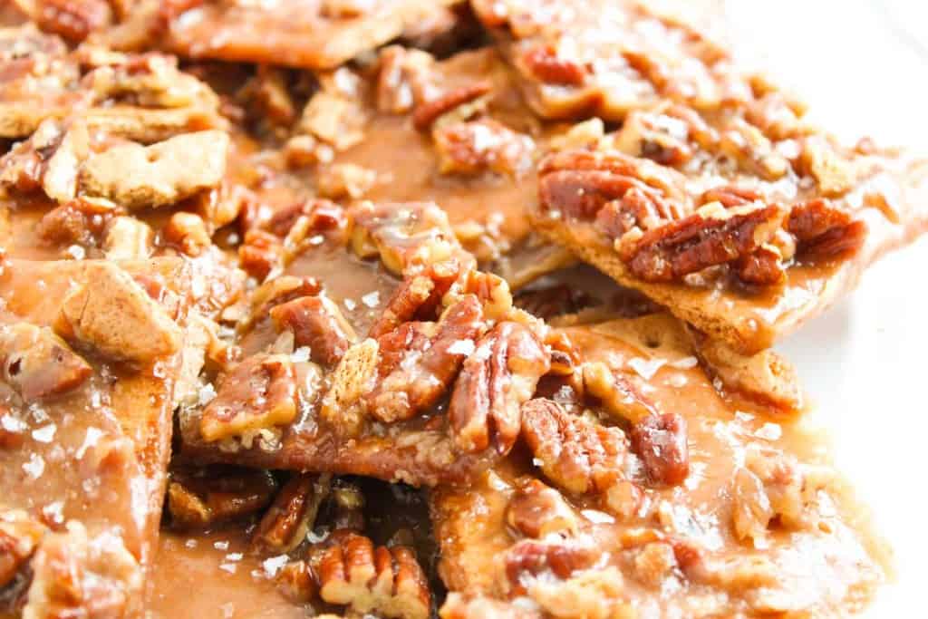 Close-up of homemade pecan brittle pieces coated in caramelized sugar, with visible pecan halves and a sprinkling of coarse salt on top.